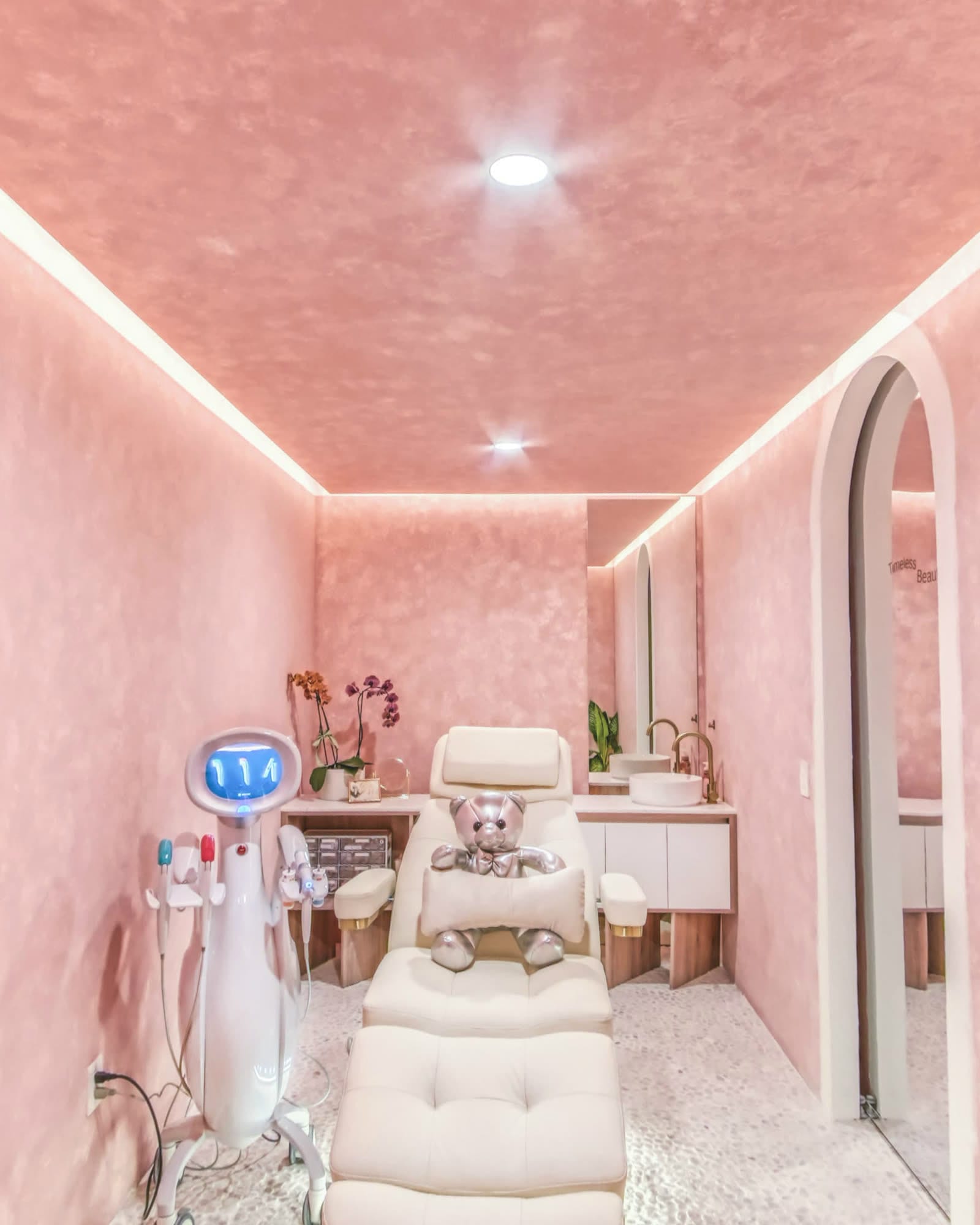 Cabina de tratamiento: sillón reclinable color crema, el equipo a un lado, orquídeas sobre la cubierta y un arco que da al pasillo.
